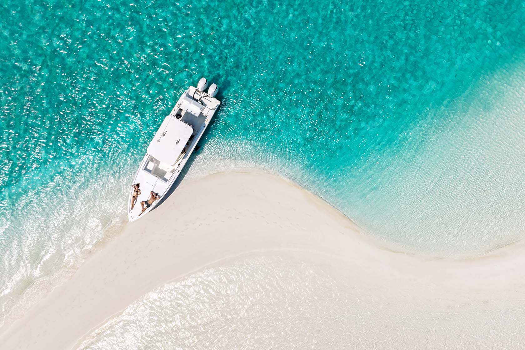 A boat resting beside a white sandbar in clear turquoise Exuma water